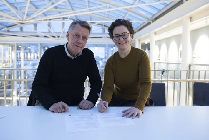 Ordfører og NAVs regiondirektør undertegner papir. Smiler mot kamera.