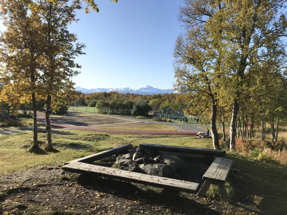 Bålplass med benker på en liten høyde med Charlottenlund aktivitets- og friluftspark i bakgrunn.