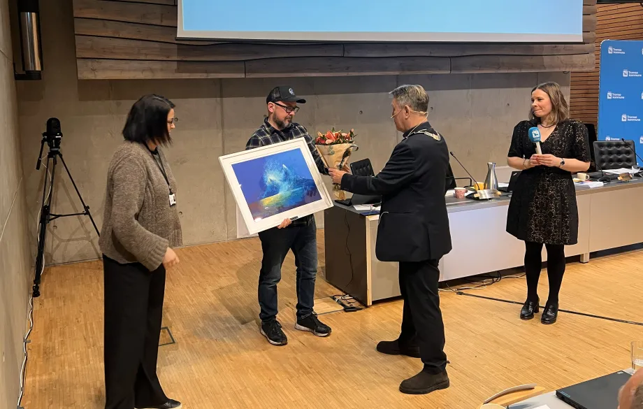 Ed Sivertsen står med kunstverk i hånda. Ordføreren overrekker han blomster.