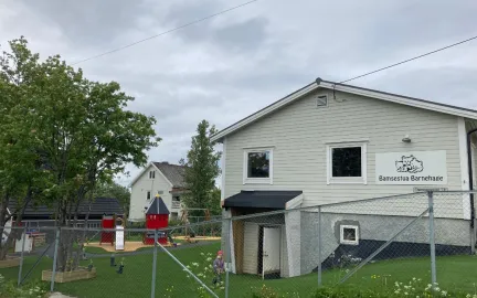 Bamsestua friluftsbarnehage sett utenfra Bamsestua friluftsbarnehage uteområde med klatretårn og grønt gress en skyet sommerdag
