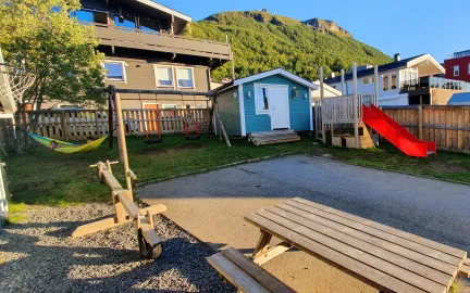 Dalen familiebarnehage uteområde Dalen familiebarnehage uteområde med lekehus, husker, benker og bord en solrik sommerdag med blå himmel
