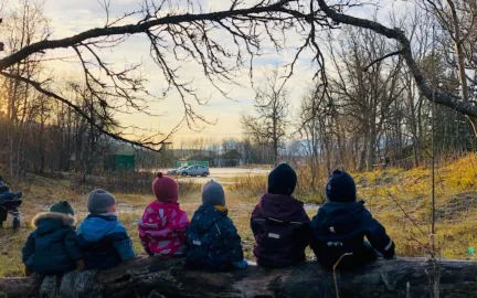 Ekrehagen friluftsbarnehage på tur Seks barn som sitter på et fallent tre i skogen en høstdag i Ekrehagen friluftsbarnehage