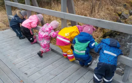 Seks barn som står på en bro og ser ned i elva ved Kattfjord barnehage