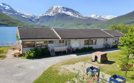 Lakselvbukt barnehage sett utenfra med lekeområde, hav og fjell en strålende sommerdag