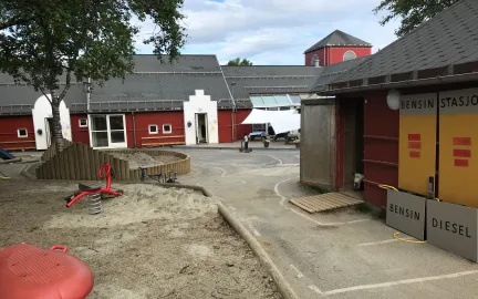 Olsgård barnehage uteområde med et stort tre, sandkasser og lekeapparater en sommerdag