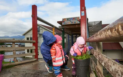 Reinen barnehage inngang med tre barn som ser på blomster i en krukke en våt sommerdag