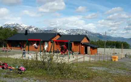 Uteområde på Skittenelv barnehage med sandkasser og husker, blå himmel en solrik sommerdag