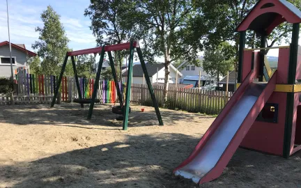 Lekeområdet i Slettaelva barnehage med høye trær, husker og klatretårn en solrik sommerdag