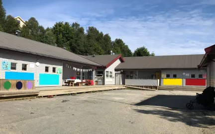 Slettaelva barnehage sett utenfra en solrik sommerdag med blå himmel og grønn skog