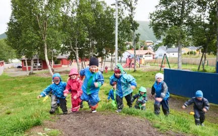 Syv barn som springer opp på en bakketopp i Tromsdalen barnehage en regntung sommerdag