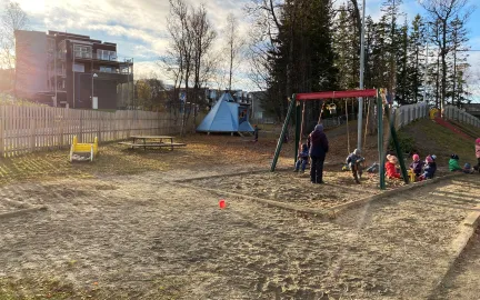 Workinnmarka barnehage uteområde med lavvo, husker og mange barn en solrik sommerdag