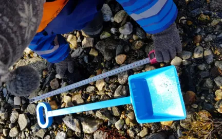 Barn som sitter i fjæra og måler en blå spade
