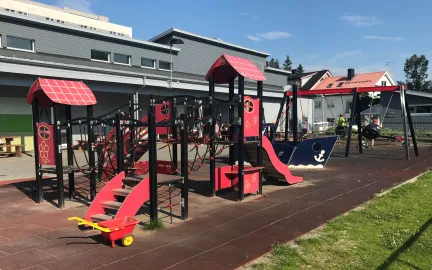 Uteområde med klatretårn, sjørøverskute og grønt gress en sommerdag med blå himmel