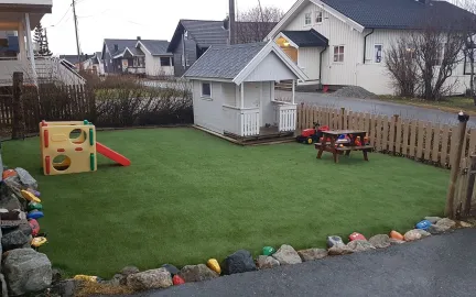 Lekestua familiebarnehage Lekeområdet i hagen med dukkehus, sklie, benk og bord på grønt gress en sommerdag