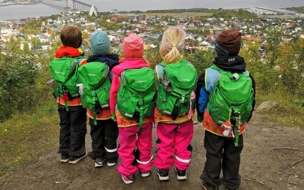 Fem barnehagebarn med grønne ryggsekker på fjelltur med utsikt over Tromsøya en sommerdag 