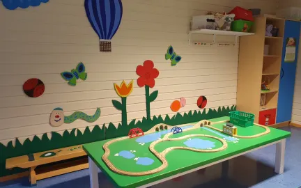 Norlandia Kvitungen barnehage Lekeområde med malte blomster og luftballong på veggen og et grønt bord med togskinner i tre