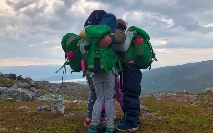Tre barn holder rundt hverandre på en fjelltopp en tidlig høstdag