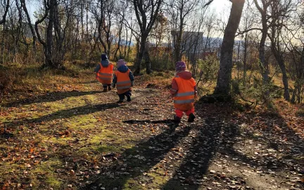 Tre barn med refleksvester på tu i skogen ved Norlandia friluftsbarnehage