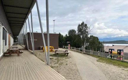 Uteområde med benker og klatretårn en sen sommerdag med skyer og blå himmel.