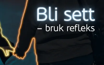 To personer som holder hender går langs mørk vei. Tekst i bildet sier: Bli sett - bruk refleks.