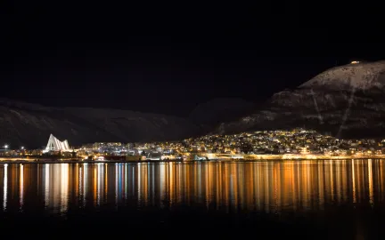 Vinterbilde av Tromsdalen, Ishavskatedralen og lysene som speiler seg i Tromsøysundet. 