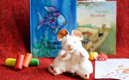 Barnebok, musebamse, tegnestifter og tegneark på rød duk.