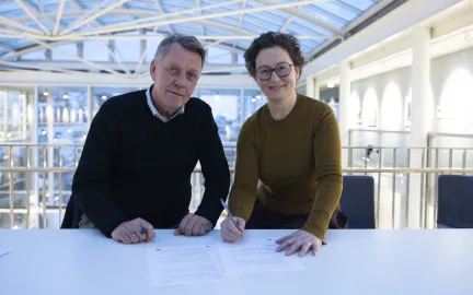 Ordfører og NAVs regiondirektør undertegner papir. Smiler mot kamera.
