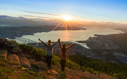 Bilde av Tromsø by, sett fra fjellheisen, to mennesker som strekker hender i været, solnedgang Tromsø by sett fra fjellehisen
