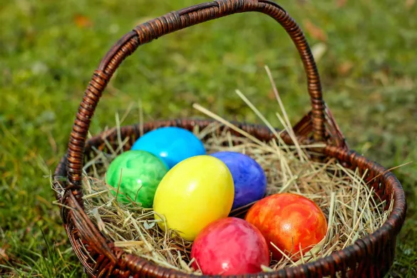 Egg malt i ulike farger ligger i en brun kurv. Grønt gress i bakgrunnen. Foto.