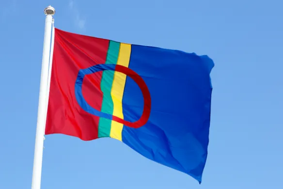 Det samiske flagget på flaggstang mot blå himmel. Foto.