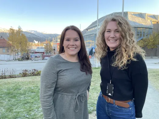 Sigrid Mogård-Jansen (til venstre) og Helga Bårdsdatter Kristiansen Sigrid Mogård-Jansen, til venstre, og Helga Bårdsdatter Kristiansen fra Tromsø kommune står på plenen utenfor rådhuset, og smiler mot kamera.