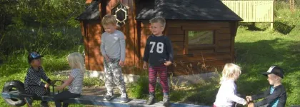 Bjerkaker barnehage uteområde med lekehus og seks barn på en huske en sommerdag med grønt gress