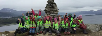 Flere barn med grønne refleksvester fra Karveslettlia barnehage på tur på en fjelltopp en grå høstdag