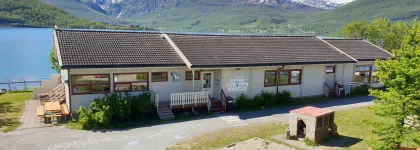Lakselvbukt barnehage sett utenfra med lekeområde, hav og fjell en strålende sommerdag