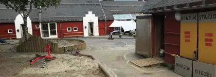 Olsgård barnehage uteområde med et stort tre, sandkasser og lekeapparater en sommerdag