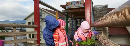 Reinen barnehage inngang med tre barn som ser på blomster i en krukke en våt sommerdag