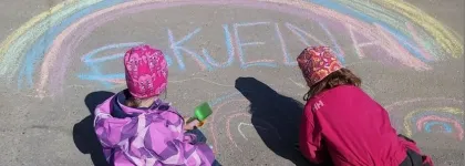 To barn tegner regnbue med kritt i barnehagens uteområde en solrik sommerdag