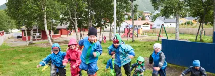 Syv barn som springer opp på en bakketopp i Tromsdalen barnehage en regntung sommerdag