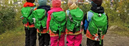 Fem barnehagebarn med grønne ryggsekker på fjelltur med utsikt over Tromsøya en sommerdag 