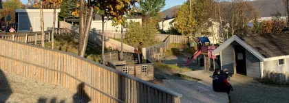 Gimle studentbarnehage med lekeområde sett utenfra en sommerdag med blå himmel